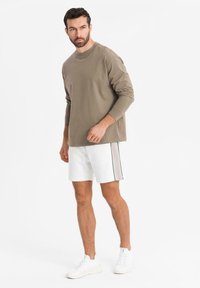 Kaki langærmet skjorte, hvide shorts med side sort stribe og hvide sneakers. Simpelt design uden synlige mønstre eller detaljer.