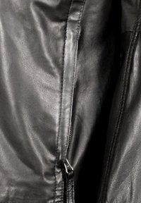 Zwarte leren jas met een gladde textuur, een zichtbare rits aan de zijkant en iets kreukelig stof voor een getailleerde silhouet.