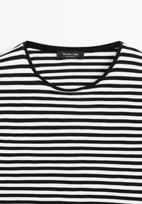 Czarna i biała koszulka w paski z okrągłym dekoltem i żebrowaną teksturą. Metka informuje, że jest marki "Massimo Dutti" i została wyprodukowana w Maroku.