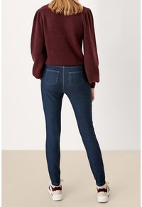 Vínový texturovaný svetr s nabíranými rukávy, doplněný tmavě modrými skinny džínami a bílými teniskami s burgundskými akcenty.