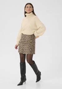 Suéter de cuello alto de color crema, textura de punto oversize; falda corta de leopardo; botas de cuero negras hasta la rodilla con punta afilada; medias transparentes.