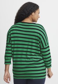 Zeleni in črni prugasti oversized pulover, ki ima tri četrtinske rokave in okrogel dekolte, izdelan iz mehkega, lahkega materiala.