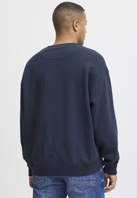 Marineblauwe sweatshirt met een ronde hals, verlaagde schouders en geribbelde boorden. Gemaakt van zacht materiaal, heeft een ontspannen pasvorm en een effen kleur.