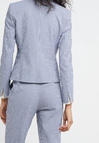 Sukně a blejzr v modro-bílé kostičky, s přiléhavým blejzrem s peplum pasem a na míru šitými kalhotami. Hladká textura, strukturovaný design.