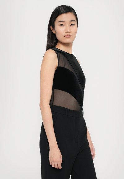 Black bodysuit featuring a mix of sheer and velvet panels in angular design, paired with black tailored trousers. Smooth texture and fitted style.