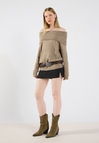 Off-shoulder beige strikkegenser, kombinert med et svart miniskjørt med sideslisser, og olivengrønne ankelboots i semsket skinn.