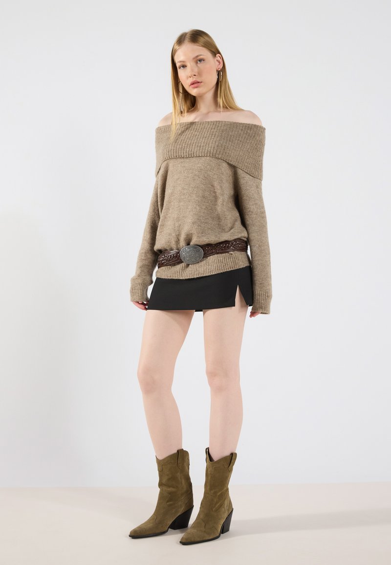 Sweter beżowy, dzianinowy, z opuszczonymi ramionami, zestawiony z czarną mini spódnicą z bocznymi rozcięciami oraz oliwkowymi zamszowymi botkami na obcasie.