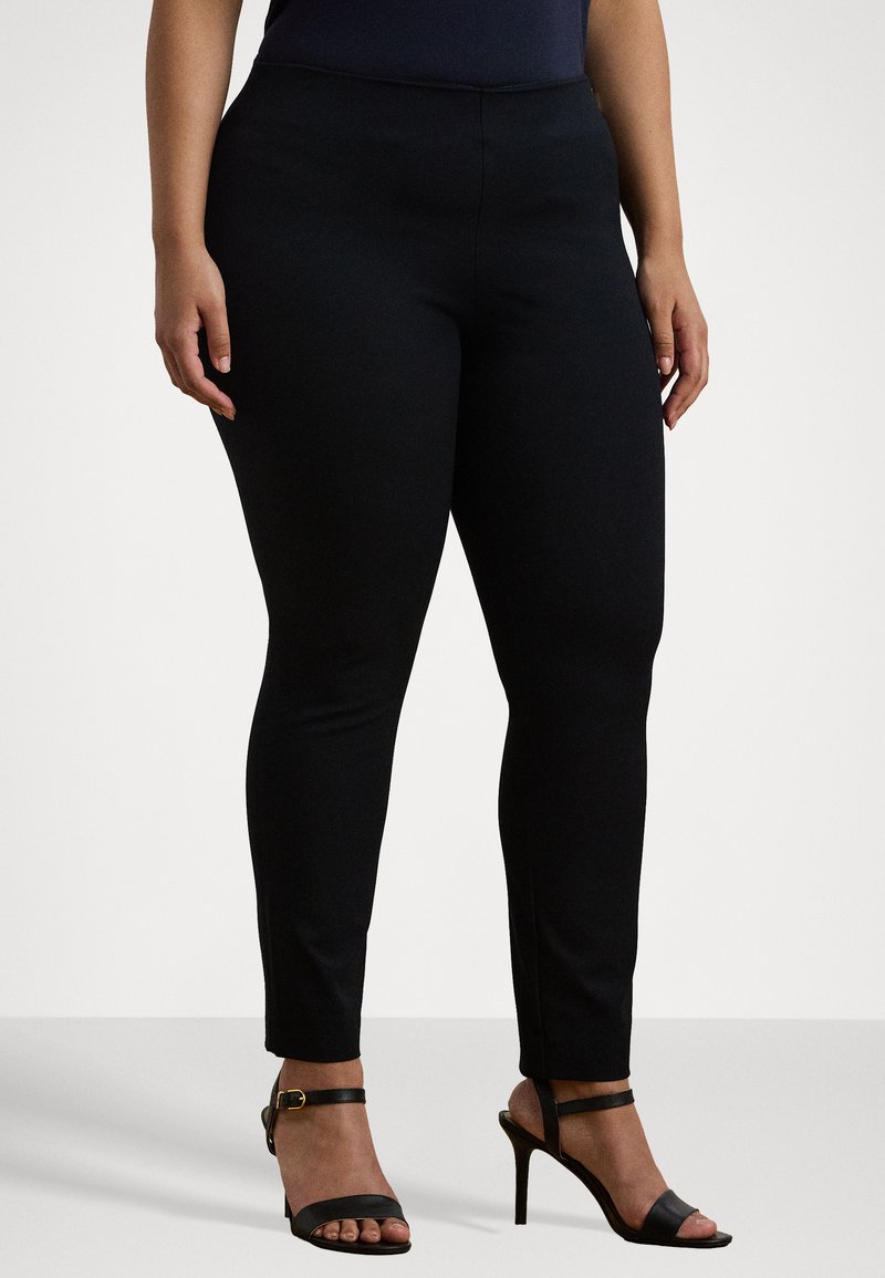 Pantalons noirs ajustés en matériau extensible. Le design présente une taille haute et une coupe fuselée, associés à des sandales noires à talons hauts.