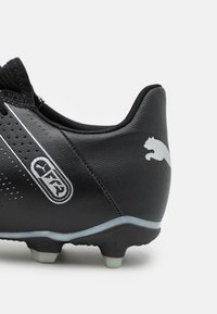 Botín de fútbol negro con parte superior sintética texturizada, acentos en blanco y un logo en el talón. Presenta tachuelas cónicas para tracción.