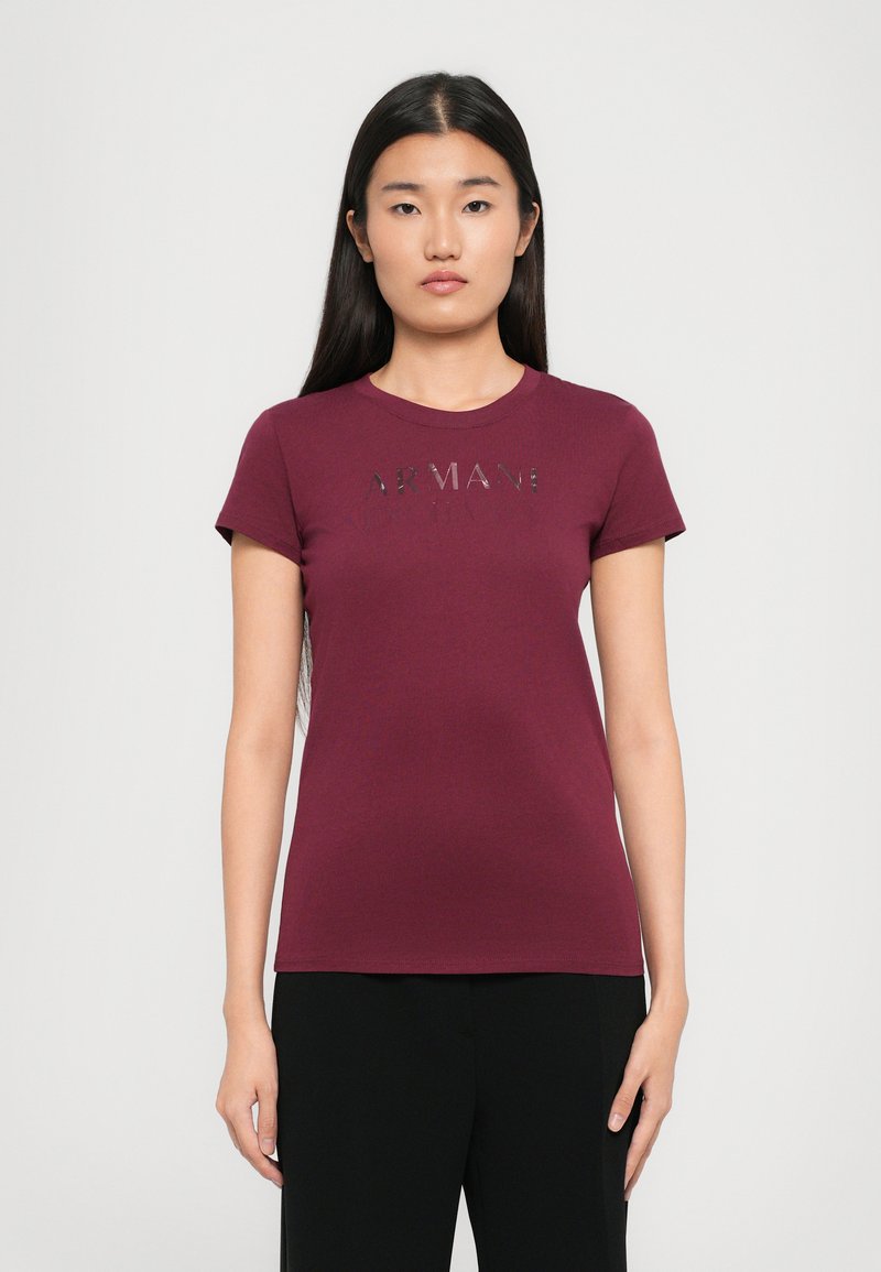 Bordeaux T-Shirt aus weichem Baumwollmaterial mit kurzen Ärmeln, auf der Brust mit dem Wort "ARMANI" in einem glänzenden, reflektierenden Design versehen.