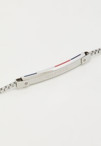 Sølv-tone armbånd med en glat metalrem, der har blå, hvide og røde vandrette accenter. Ledkæde design med indgraveret brandlogo.