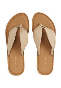Beige kankaan flip-flops yang mempunyai tali simpul, tapak kaki dari kulit coklat, dan tepi yang dijahit. Aksen logo emas pada tali.