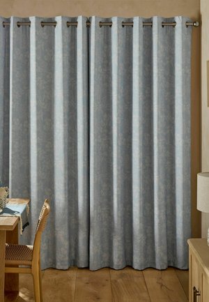Hellblaue florale Vorhänge, die an einer Metallvorhangstange in einem Raum mit Holzboden und teilweise sichtbaren Holzmöbeln hängen.