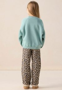 Sweatshirt vert menthe avec un col rond, associé à un pantalon ample beige et marron à imprimé léopard et des chaussures légères marron.