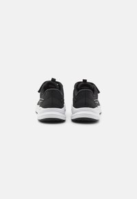 Chaussures de sport noires avec une tige en maille texturée, semelle blanche en coussinage et détail de logo contrastant. Vue arrière montrant la languette au niveau du talon.