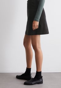 Zwarte corduroy A-lijn rok, gecombineerd met een groene langemouwen top, zwarte sokken en zwarte instapschoenen. Soepele textuur, eenvoudig ontwerp.