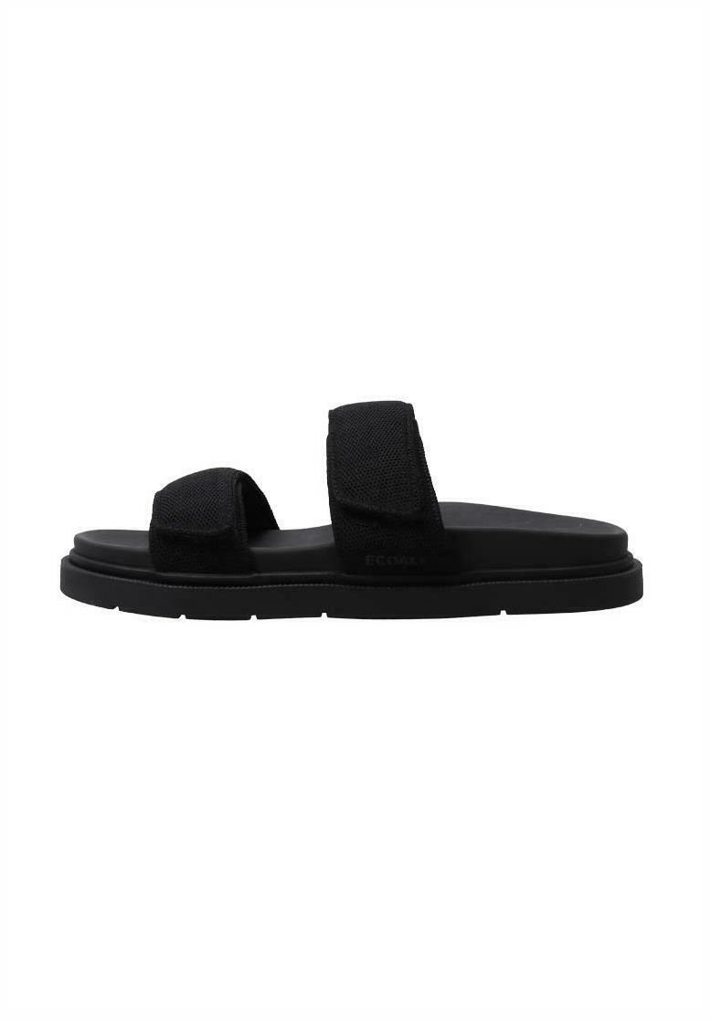 Sandalia plana negra con dos correas ajustables. Hecha de tela suave. Cuenta con una suela plana y un diseño minimalista. Textura ligera.