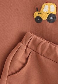 Roestkleurig t-shirt met een geborduurde, gestructureerde gele tractor en zwarte wielen, gecombineerd met bijpassende roestkleurige broek met een geraffineerde taille en zak.