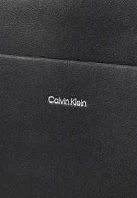 Portafoglio in pelle nera con una texture liscia, caratterizzato da un design cucito e un discreto logo bianco "Calvin Klein" sulla parte anteriore.