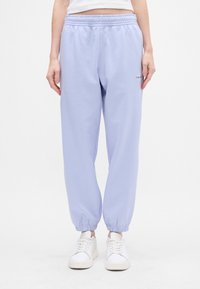 Heled lavendlisemed jalgadega püksid elastse vöökoha ja mansettidega. Vasakul reitel on tikandiga logo. Materjal näeb välja pehme ja sile.