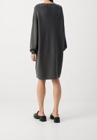 Robe-pull grise oversize à manches longues, col côtelé et texture douce. Associée à des mules noires à talons épais.