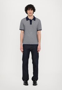 Polo triko s šedým vzorovaným designem, navy límcem a manžetami, spárováno s tmavě modrými džíny a černými botami.