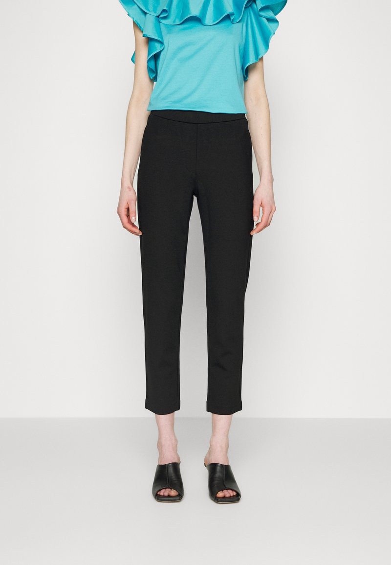 Pantalons noirs courts avec une coupe ajustée, texture lisse et une ceinture. Associés à un top turquoise à volants et des sandales noires à enfiler.