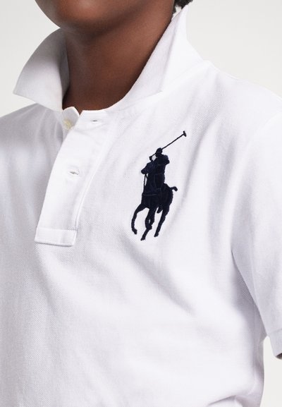 Balta polo krekls ar salocītu apkakli un divu pogu aizdares joslu. Kreisajā krūtīs izšūta tumši zila polo logotips. Izgatavots no kokvilnas materiāla.
