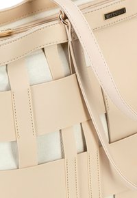 Beżowa skórzana torebka z plecionymi akcentami, z górnym zamknięciem na suwak i cienkim paskiem na ramię. Zawiera logo marki po boku.