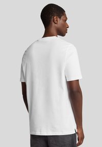 Hvid bomulds T-shirt med korte ærmer, rund halsudskæring og en afslappet pasform. Har sideskårne slidsjer i kanten for nem bevægelse.