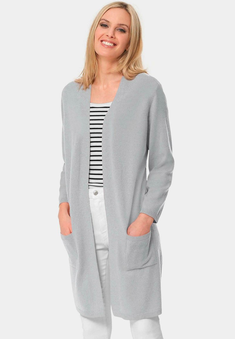 Lichtgrijze lange cardigan met een v-hals, driekwartmouwen, geribde manchetten en twee voorzakken. Gedragen over een gestreept topje.