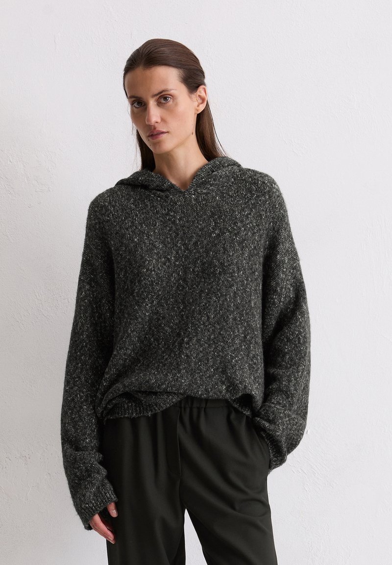 Hoodie en tricot gris foncé avec une coupe décontractée, des poignets et un ourlet côtelés. Porté sur un pantalon noir ; matériau texturé avec une finition douce.