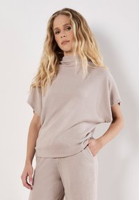 Jasnobeżowy sweter prążkowany z wysokim dekoltem i krótkimi rękawami, w połączeniu z dopasowanymi spodniami prążkowanymi, o luźnym, swobodnym kroju.
