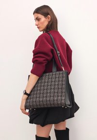 Sort og mønstret tote taske med en struktureret form, der har et dekorativt design, læderkanter og hardware-accenter i guld.