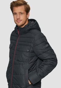 Zwarte gewatteerde jas met capuchon, voorzien van een ritssluiting, twee borstzakken en rode accenten. Textuurstof met een gladde afwerking.