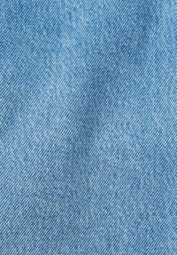 Gros plan sur un tissu en denim bleu clair montrant une texture de tissage diagonal et des variations de couleur naturelles.
