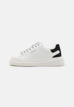 Hvide lædersneakers med sort ruskindsaftapning, teksturerede snørebånd og tyk hvid sål. "GUESS" brandingen er tydeligt vist på siden.