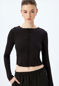 Zwarte langärmige crop top van ribbelstof, met een onafgewerkte zoom en een detail met een middennaad, gecombineerd met relaxed zittende zwarte broek.