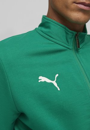 Groene zip-up jack gemaakt van gladde stof. Heeft een hoge kraag en een wit Puma-logo op de linkerborst. Opvallende rits vermeld.
