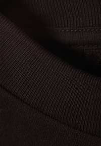 Gros plan sur un tissu à côtes sombres avec un bord plié montrant la texture de tricot et les détails de couture.