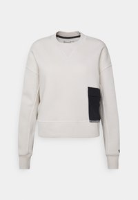 Sudadera de color beige claro con cuello redondo, mangas largas y un bolsillo lateral negro. Incluye puños y dobladillo acanalados.