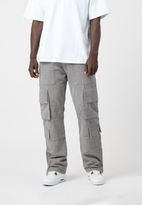Pantalon cargo gris avec plusieurs grandes poches, une coupe décontractée et un tissu résistant. Assorti à un t-shirt blanc et des baskets blanches.