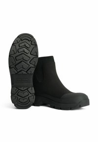Botas de tobillo negras hechas de goma con una superficie exterior texturizada, paneles laterales elásticos y una suela rugosa y con patrón para mayor tracción.