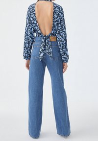 Blouse à manches longues florale avec dos ouvert et détail noué, associée à un jean large taille haute en denim bleu avec une étiquette contrastante.