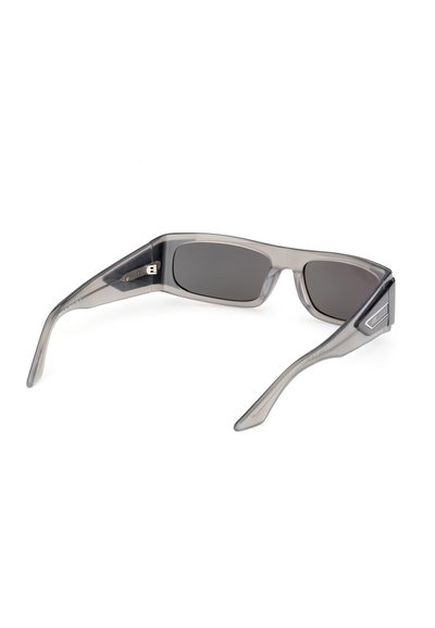 Lunettes de soleil rectangulaires translucides grises avec des verres foncés, ouvertes et posées sur une surface blanche, montrant l'intérieur de la monture et les charnières.