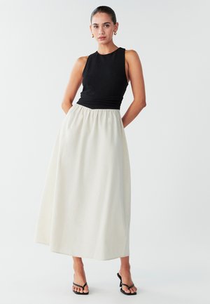 Zwart geribd mouwloos topje gecombineerd met een vloeiende, crèmekleurige maxi-rok. De rok heeft een elastische tailleband en een gladde textuur.