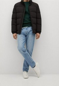 Schwarze Pufferjacke, grüner Pullover, hellblaue Jeans und weiße Sneakers. Glatte Texturen mit einer figurbetonten Silhouette und Reißverschluss.