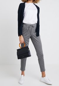 Grå joggers med dragsnodd i midjan, vit t-shirt, marinblå kardigan och svart handväska med sköldpaddsmönstrad handtag; vita sneakers på fötterna.