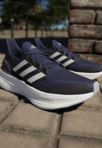 Zapatillas de running en color navy con diseño de tres rayas grises, parte superior de malla transpirable y suela acolchada blanca. Presenta acentos texturizados y cierre de cordones.