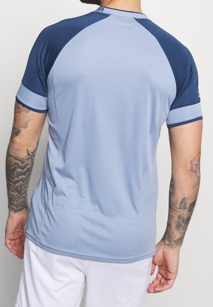 Camiseta deportiva de manga corta en azul claro con detalles en azul oscuro. Fabricada con un tejido liso y elástico; presenta mangas raglán y costuras planas.